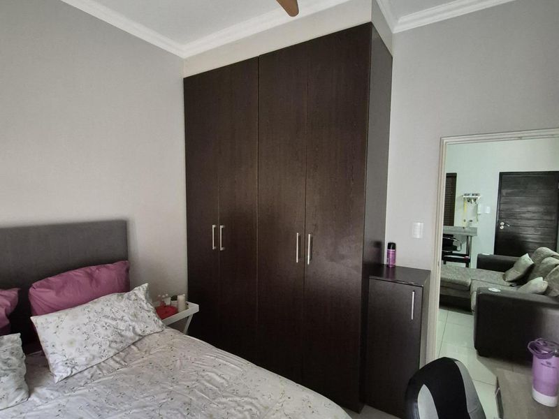 A well-maintained bedroom featuring built-in dark wood cabinetry, a ceiling fan, and tiled flooring, with an adjacent view into the living area.
