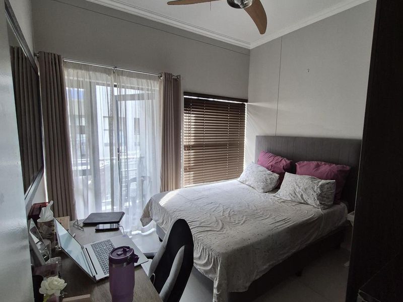 A well-lit bedroom featuring tiled flooring, a ceiling fan, and direct access to a private balcony through sliding glass doors.