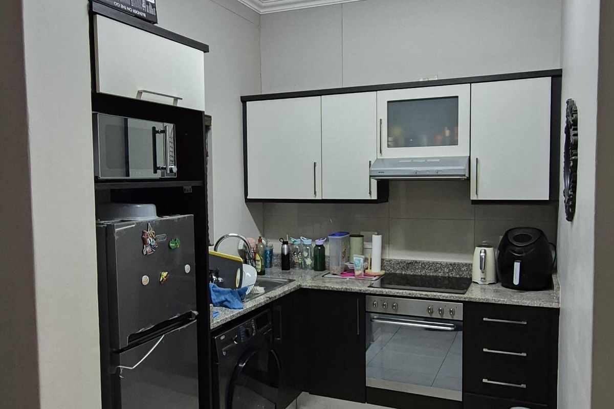Compact kitchen featuring modern two-tone cabinetry, granite countertops, built-in oven, hob, extractor fan, and integrated space for a washing machine.