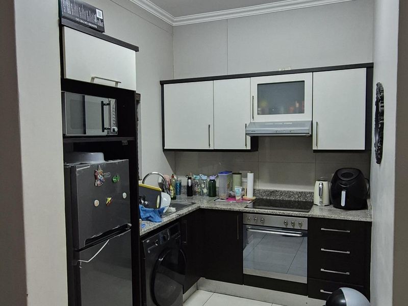 Compact kitchen featuring modern two-tone cabinetry, granite countertops, built-in oven, hob, extractor fan, and integrated space for a washing machine.