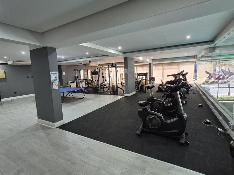 A spacious, well-lit communal gym facility featuring modern flooring, recessed ceiling lighting, and large windows providing natural light.