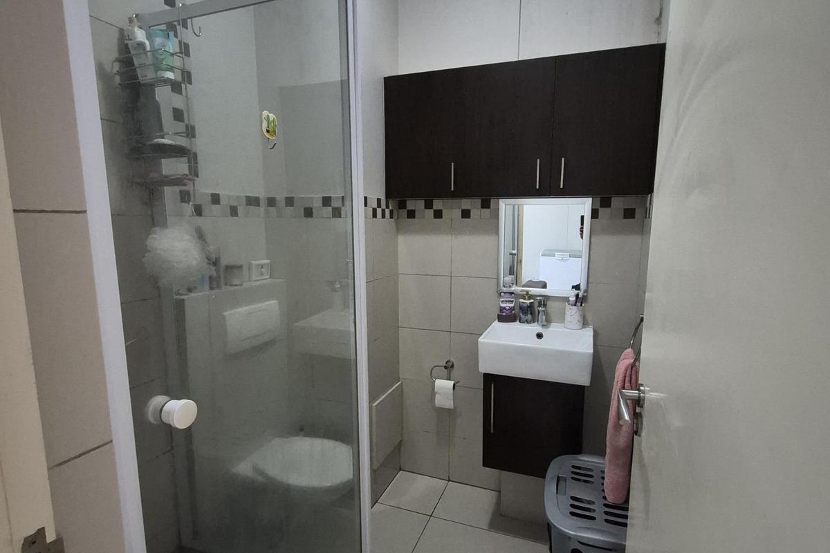 Compact bathroom featuring a glass-enclosed shower, wall-mounted vanity with storage cabinet, and tiled flooring.