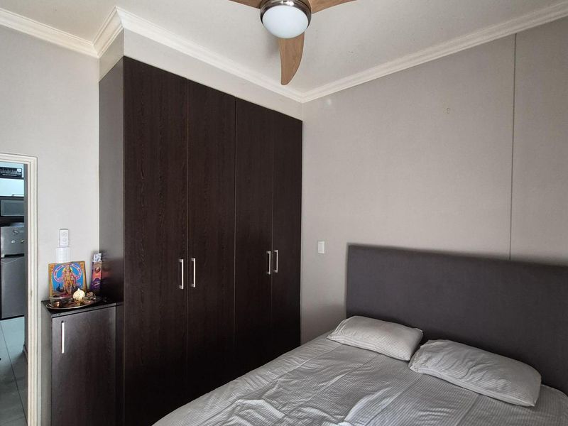 A well-maintained bedroom featuring built-in dark wood cabinetry, a modern ceiling fan, and tiled flooring.