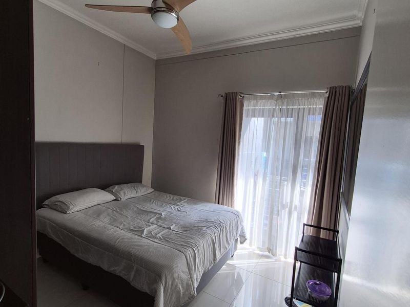 A well-lit bedroom featuring tiled flooring, a ceiling fan, and a sliding door providing access to a balcony.