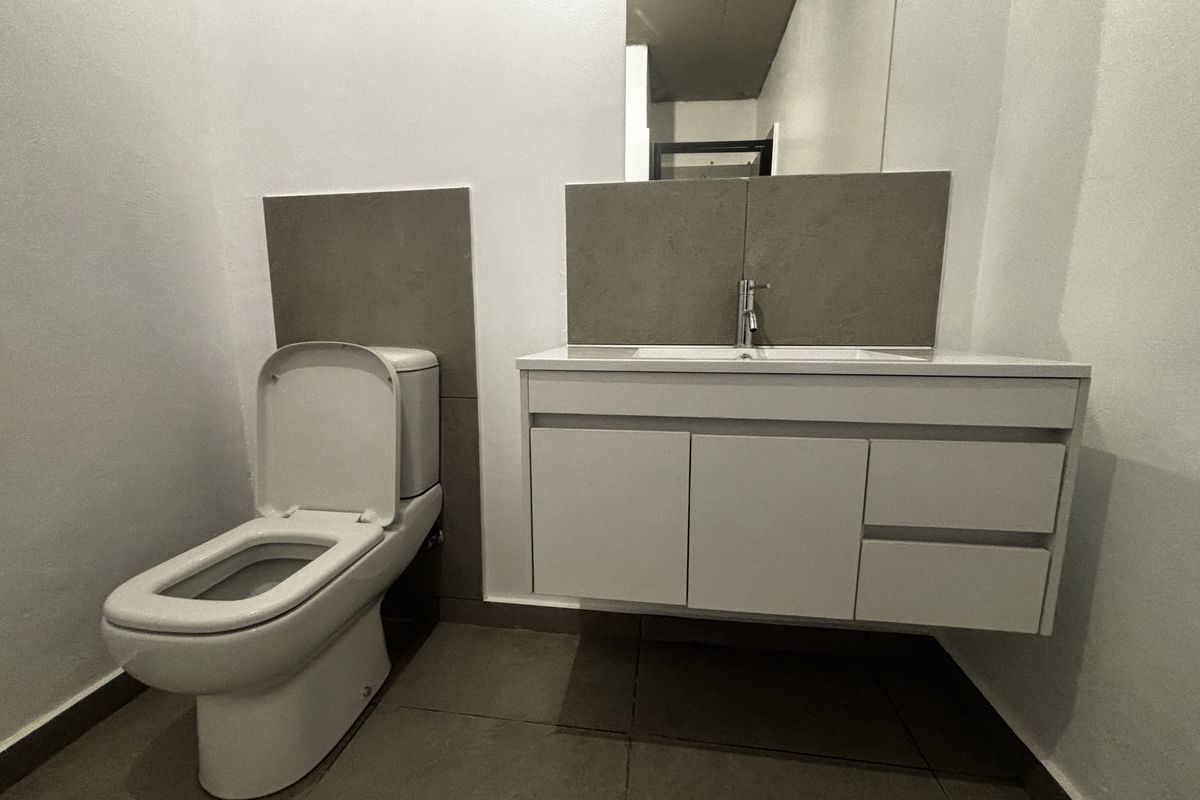 Modern bathroom featuring a wall-mounted vanity with integrated basin, large mirror, and a contemporary toilet with grey tiled flooring and splashbacks.