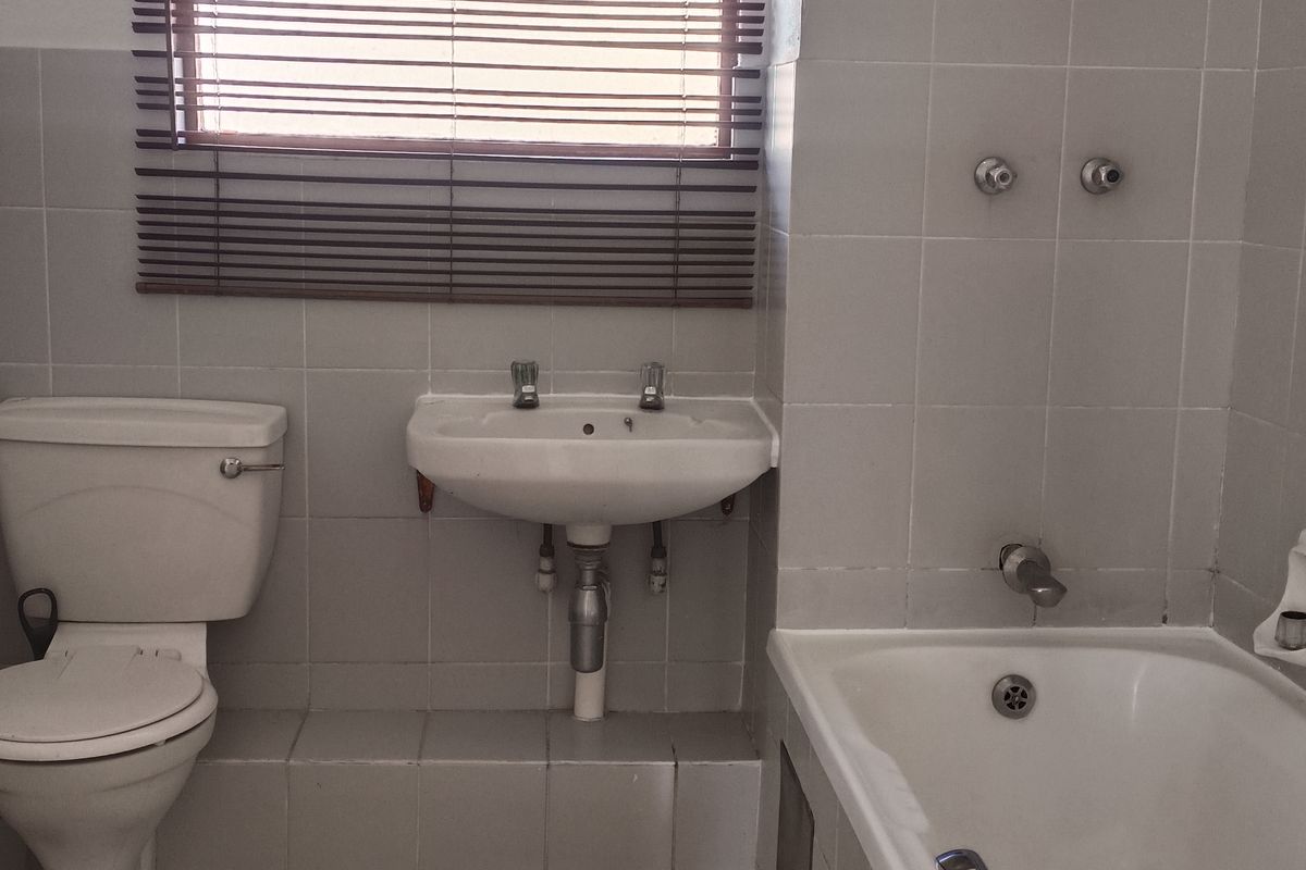 A functional bathroom featuring a standard bathtub, wall-mounted basin, and toilet with tiled walls and flooring.