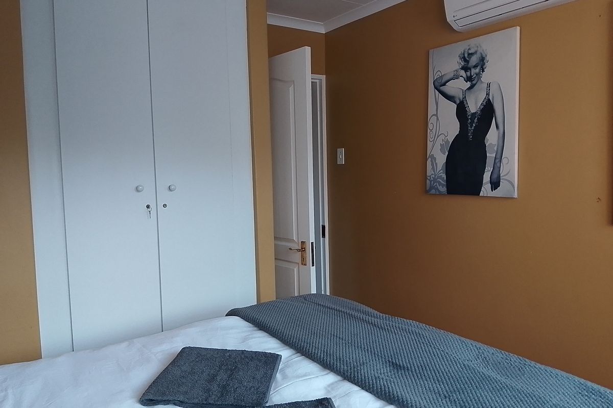 A bedroom featuring built-in cupboards, a wall-mounted air conditioning unit, and neutral wall finishes.