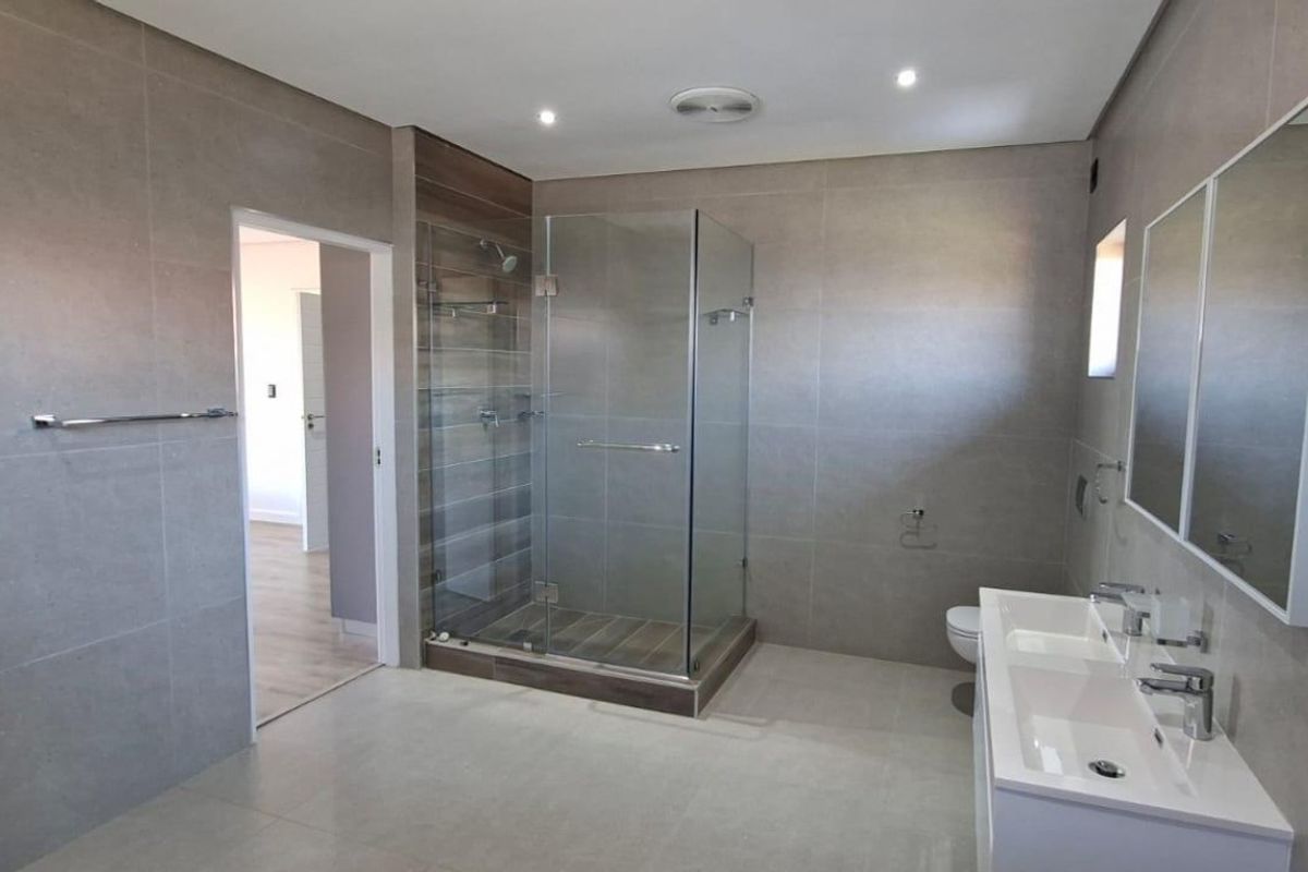 Modern bathroom featuring a glass-enclosed shower, double vanity with integrated sinks, and large-format neutral wall tiles.