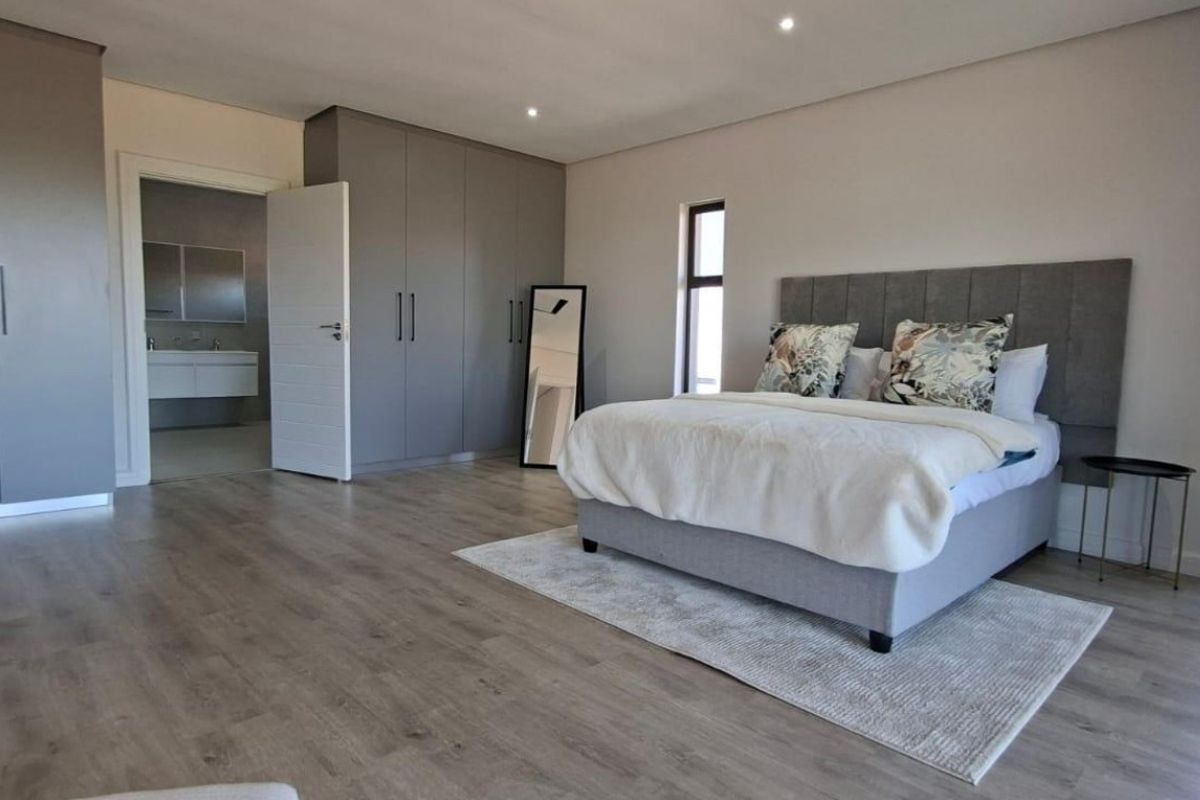 Spacious bedroom featuring modern grey built-in cupboards, light wood-look flooring, recessed ceiling lighting, and an en-suite bathroom entrance.