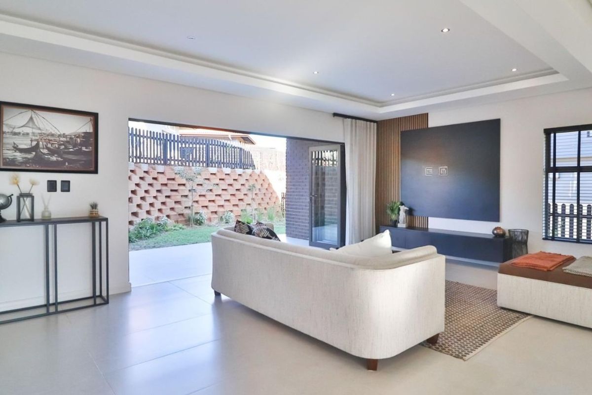 Modern open-plan living area featuring recessed ceiling lighting, sleek wall paneling, and large sliding doors opening onto a private patio and garden.