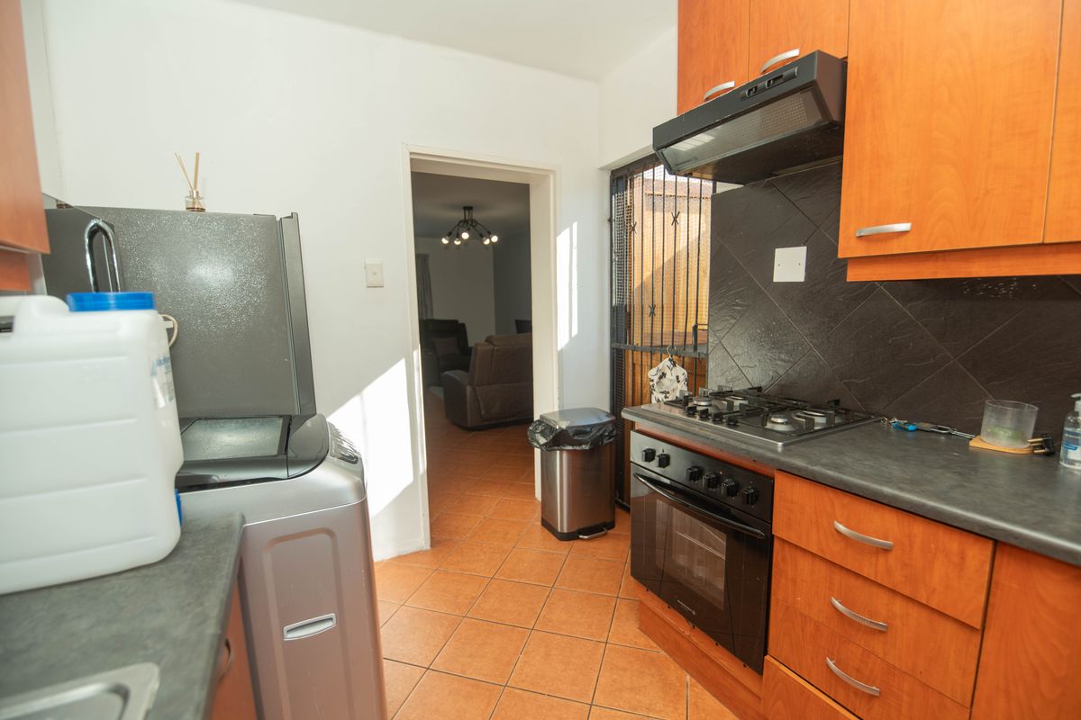 Compact kitchen featuring wooden cabinetry, built-in gas hob, oven, extractor fan, and dark tiled backsplash with direct access to the living area.