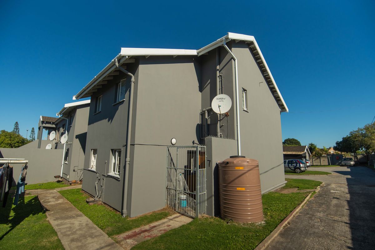 Side view of a grey townhouse featuring a water storage tank, satellite dish, and a secure gated entrance area.