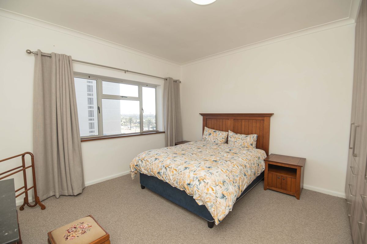A well-lit bedroom featuring neutral carpeting, built-in cupboards, and a large window offering natural light and urban views.