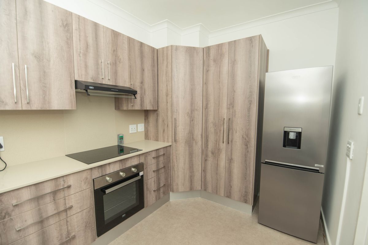 Modern kitchen featuring wood-look cabinetry, built-in oven, electric hob, extractor fan, and ample storage space.