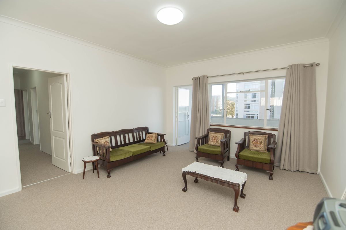 A bright and spacious living room featuring neutral carpeting, large windows with curtain tracks, and direct access to an adjoining balcony.