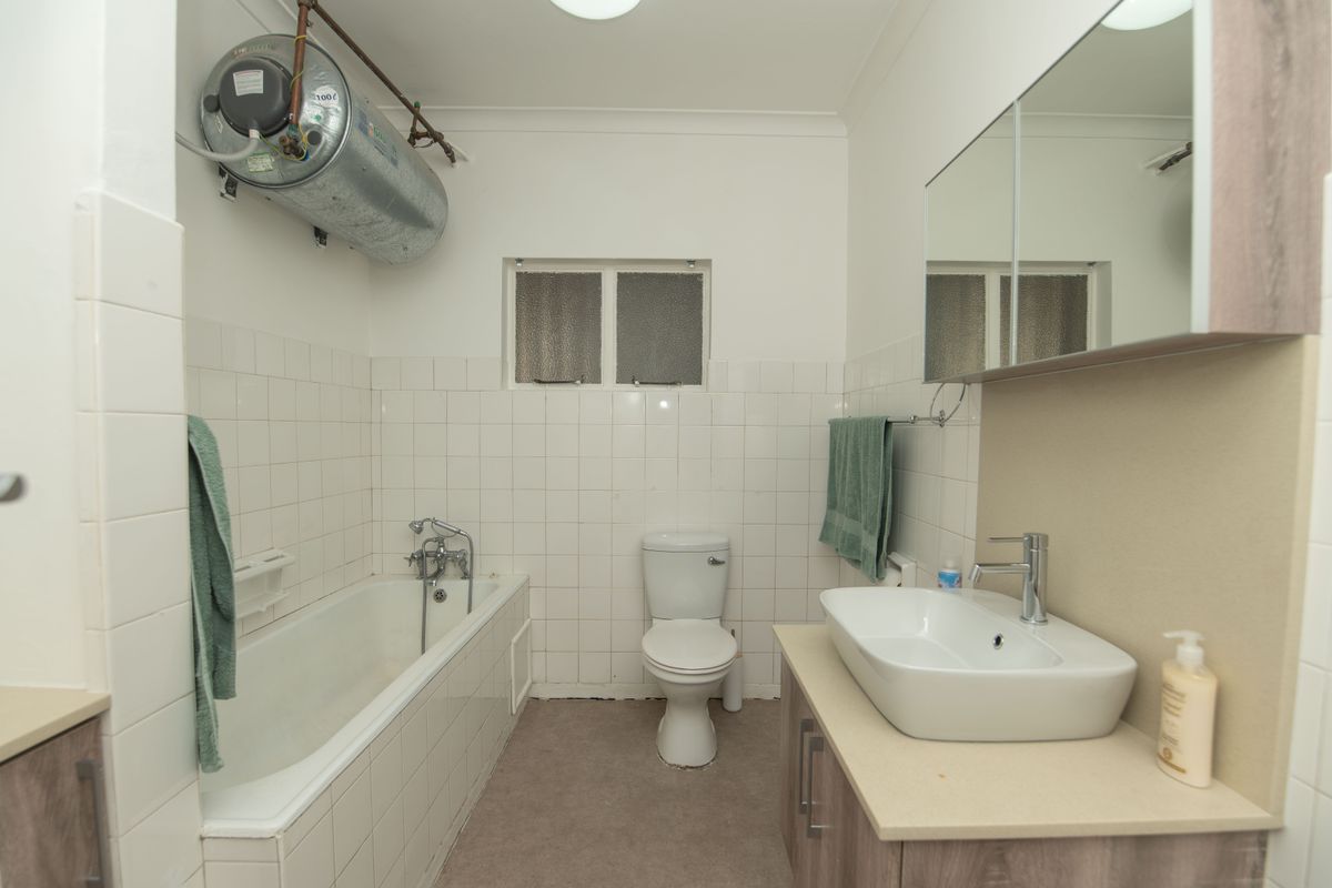 A functional bathroom featuring a bathtub with shower mixer, a vanity with basin, a wall-mounted mirror cabinet, and an exposed electric water heater.