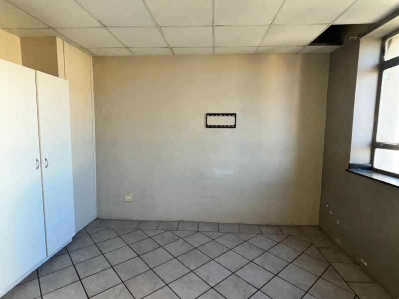 A vacant bedroom featuring tiled flooring, built-in cupboards, and a drop ceiling, offering a blank canvas for renovation.