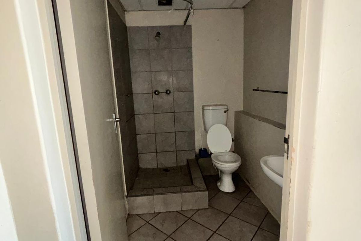 A compact bathroom featuring a tiled shower enclosure, pedestal basin, and toilet, requiring cosmetic updates and ceiling repairs.