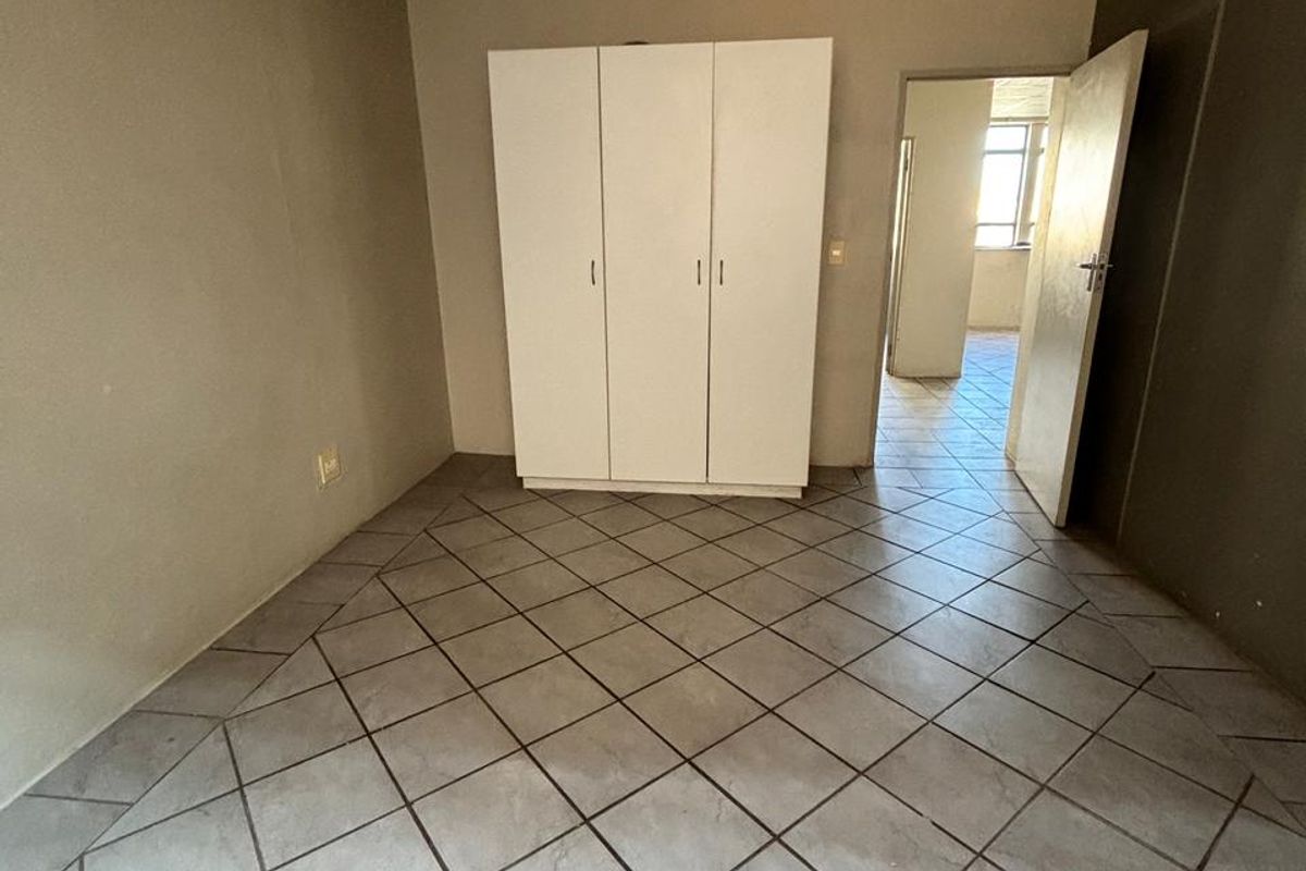 A vacant bedroom featuring tiled flooring, a built-in wardrobe, and a drop ceiling, offering a blank canvas for renovation.