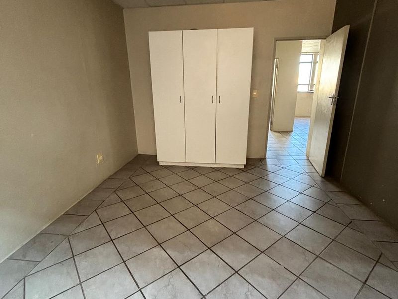 A vacant bedroom featuring tiled flooring, a built-in wardrobe, and a drop ceiling, offering a blank canvas for renovation.