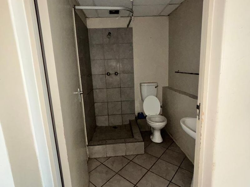 A compact bathroom featuring a tiled shower enclosure, pedestal basin, and toilet, requiring cosmetic updates and ceiling repairs.