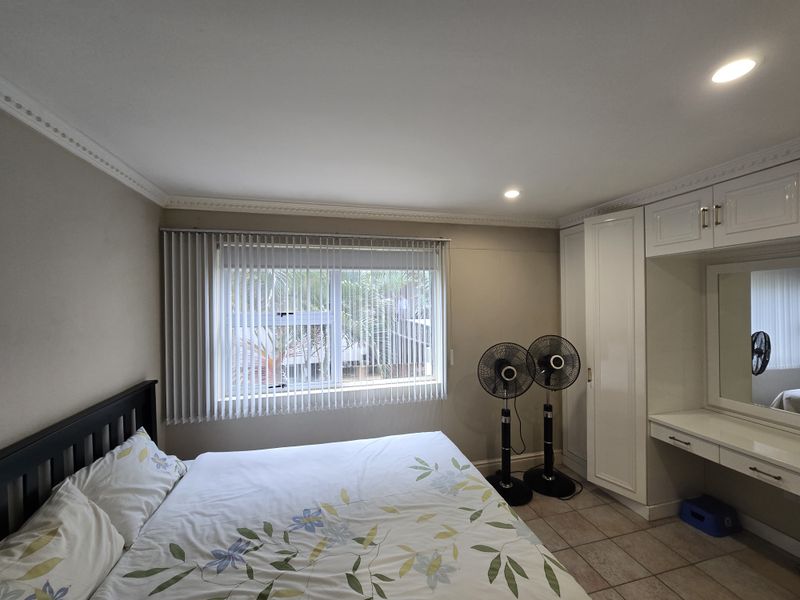 A well-maintained bedroom featuring built-in cupboards, a matching vanity unit, tiled flooring, and vertical blinds for privacy.