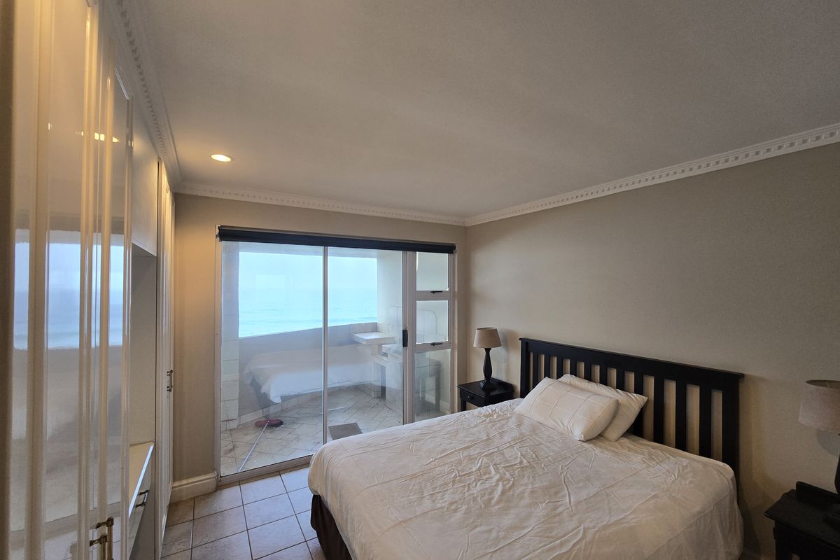 A well-maintained bedroom featuring built-in cupboards, tiled flooring, crown molding, and a sliding glass door providing access to a balcony with ocean views.