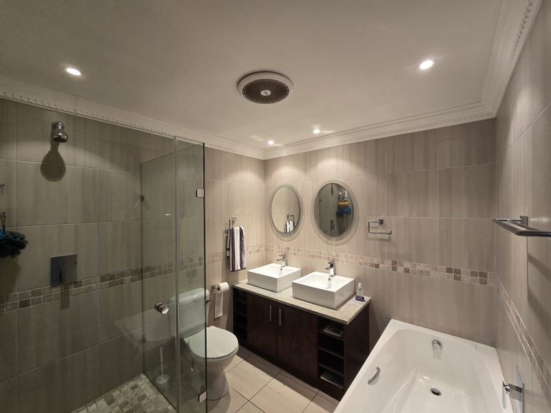 Modern bathroom featuring a double vanity with vessel sinks, a glass-enclosed shower, and a separate built-in bathtub with neutral wall and floor tiling.