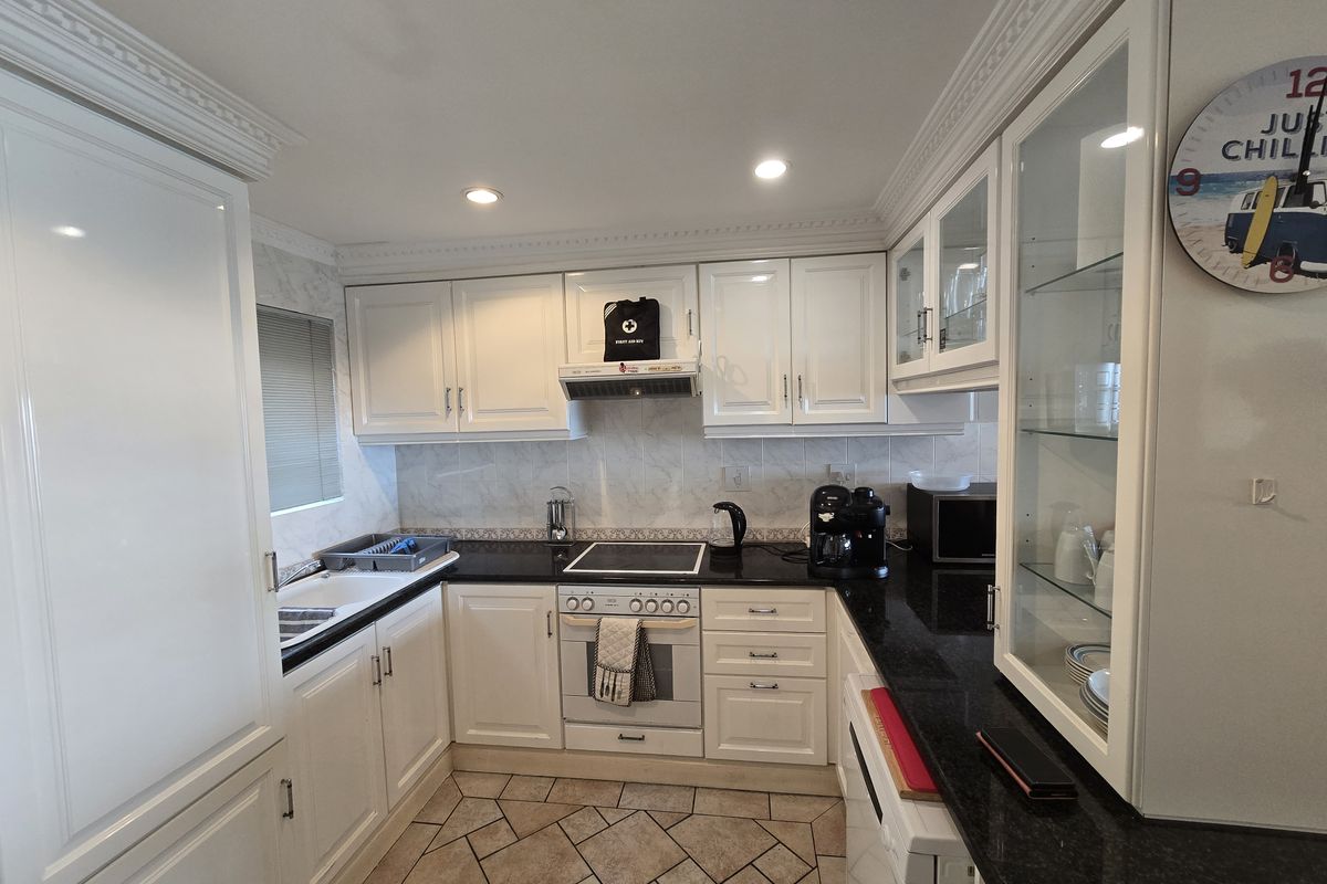 A well-maintained kitchen featuring white cabinetry, black granite countertops, an integrated oven and hob, and tiled flooring with classic coving details.