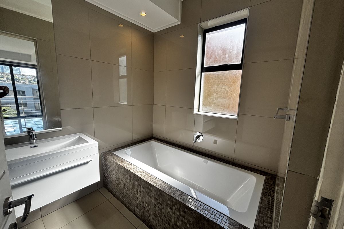 Modern bathroom featuring a built-in bathtub with mosaic tile surround, wall-mounted faucet, and a sleek floating vanity with an integrated basin.