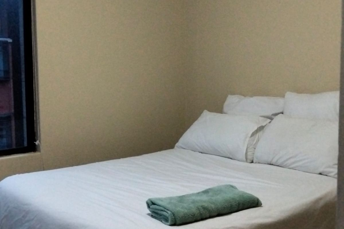 A simple bedroom featuring neutral wall tones and a window, providing a functional and quiet sleeping space.