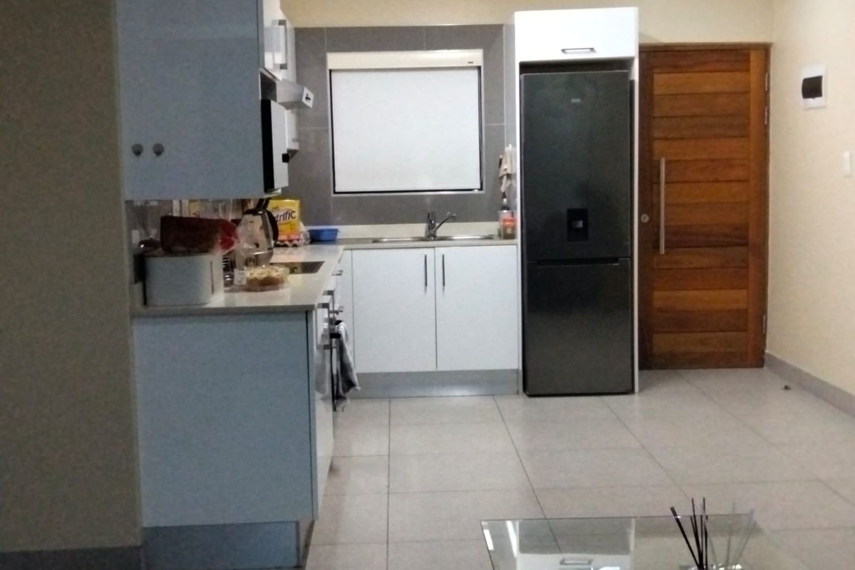 A functional kitchen featuring white cabinetry, tiled flooring, a stainless steel sink, and a modern refrigerator, adjacent to a wooden door.