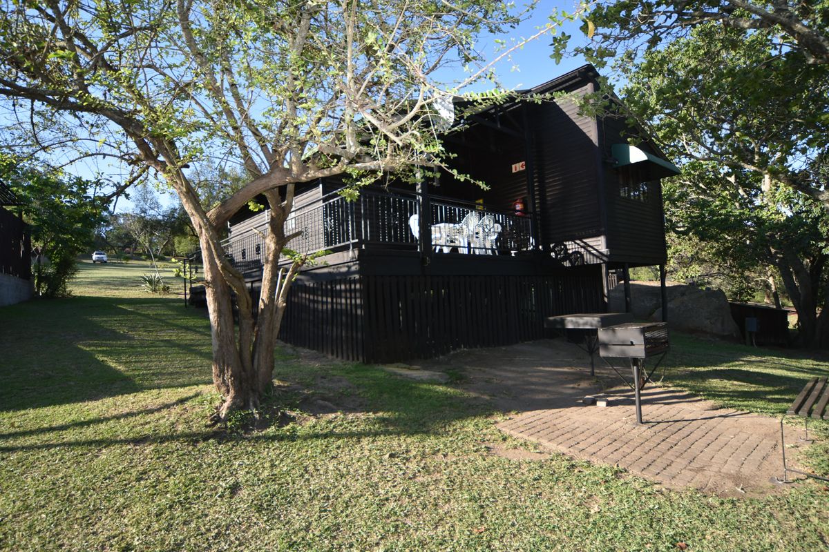 A view of the rear exterior of the property, featuring a raised wooden deck, dark timber cladding, and a paved outdoor area with a built-in braai.