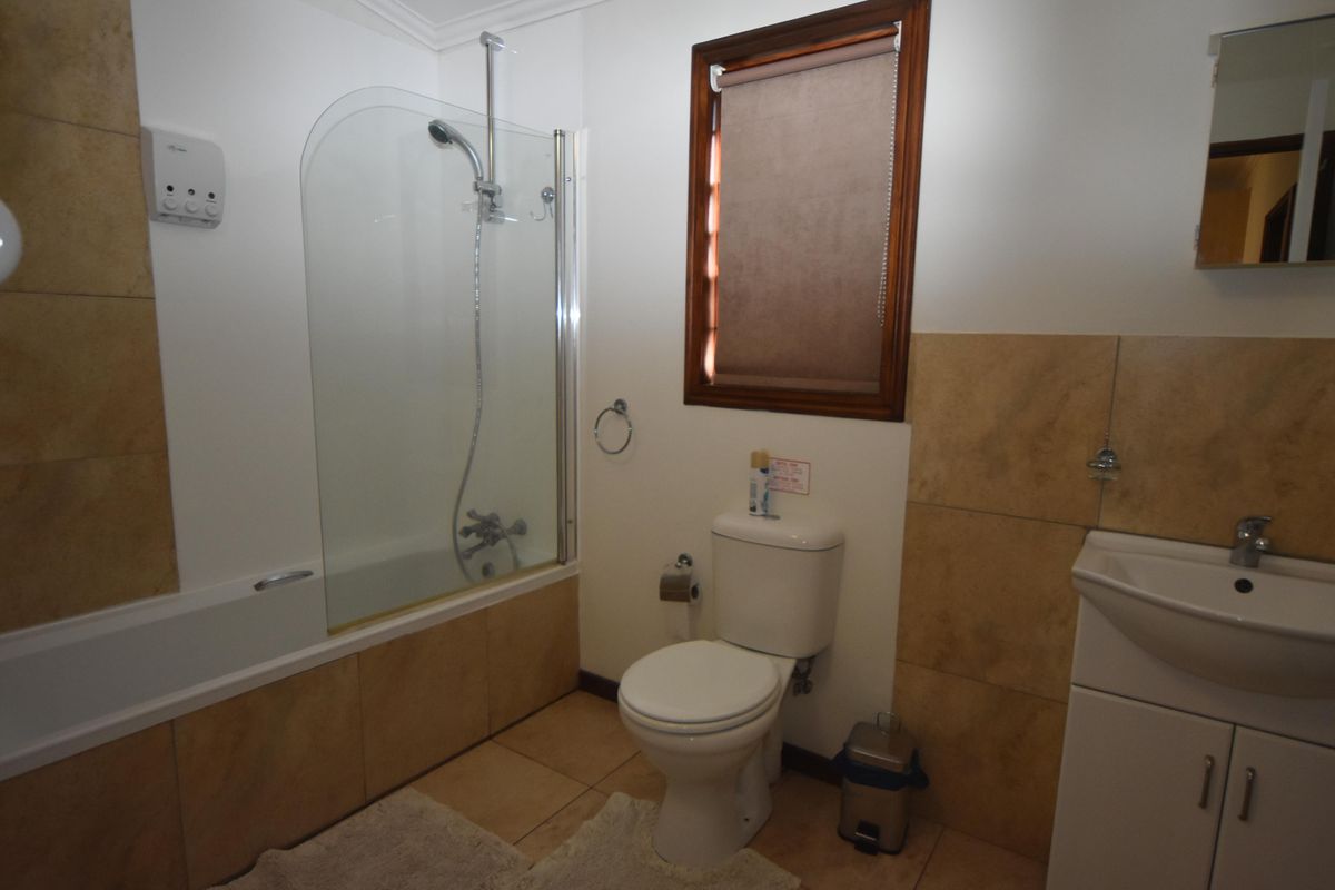 A functional bathroom featuring a shower-over-bath combination, a white ceramic toilet, and a vanity unit with integrated basin and storage.