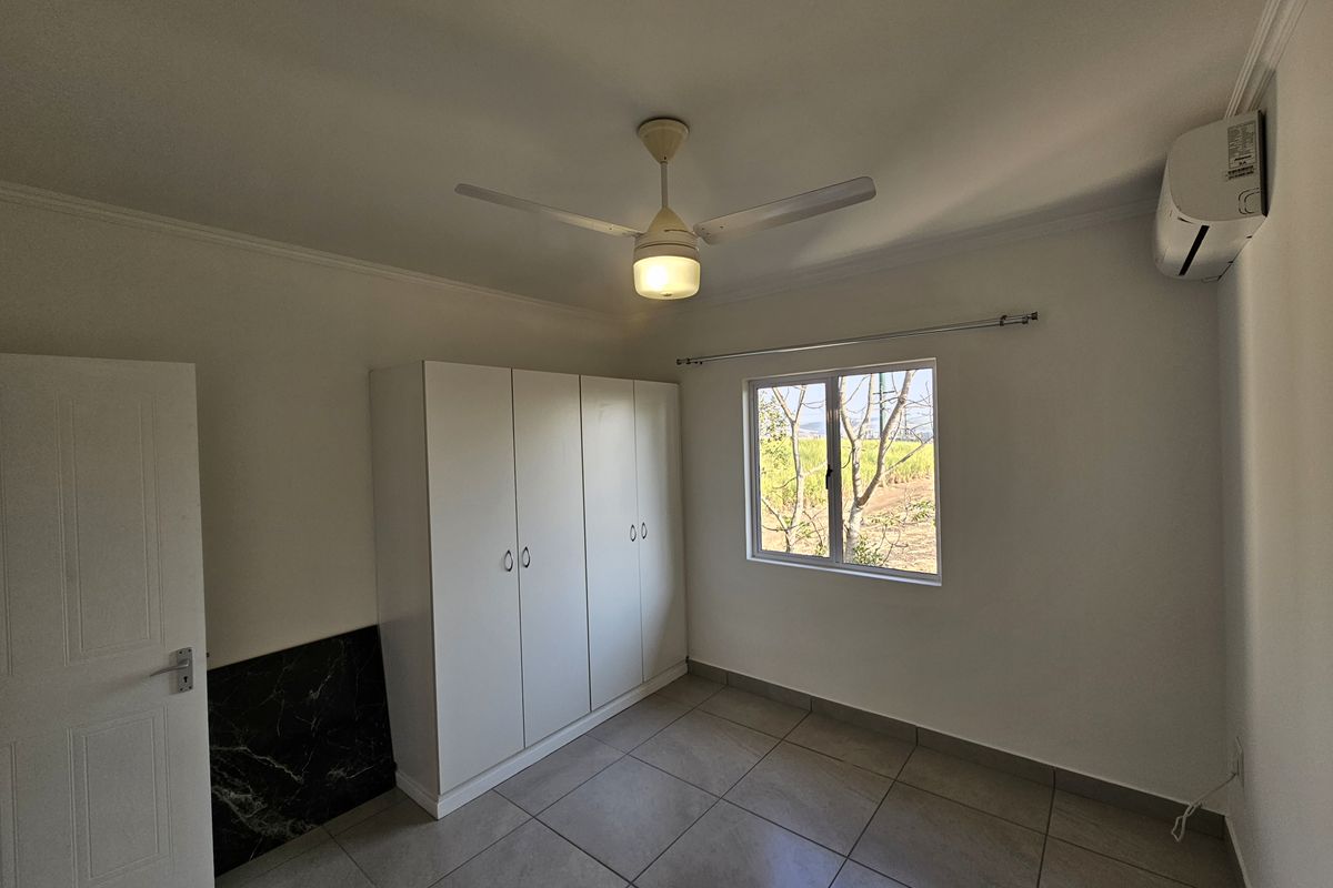 A bright bedroom featuring tiled flooring, a built-in wardrobe, a ceiling fan with integrated light, and a wall-mounted air conditioning unit.