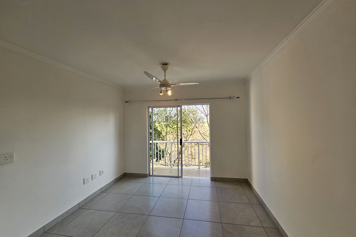 A bright, empty living room featuring neutral floor tiles, a ceiling fan, and sliding glass doors leading to a private balcony.