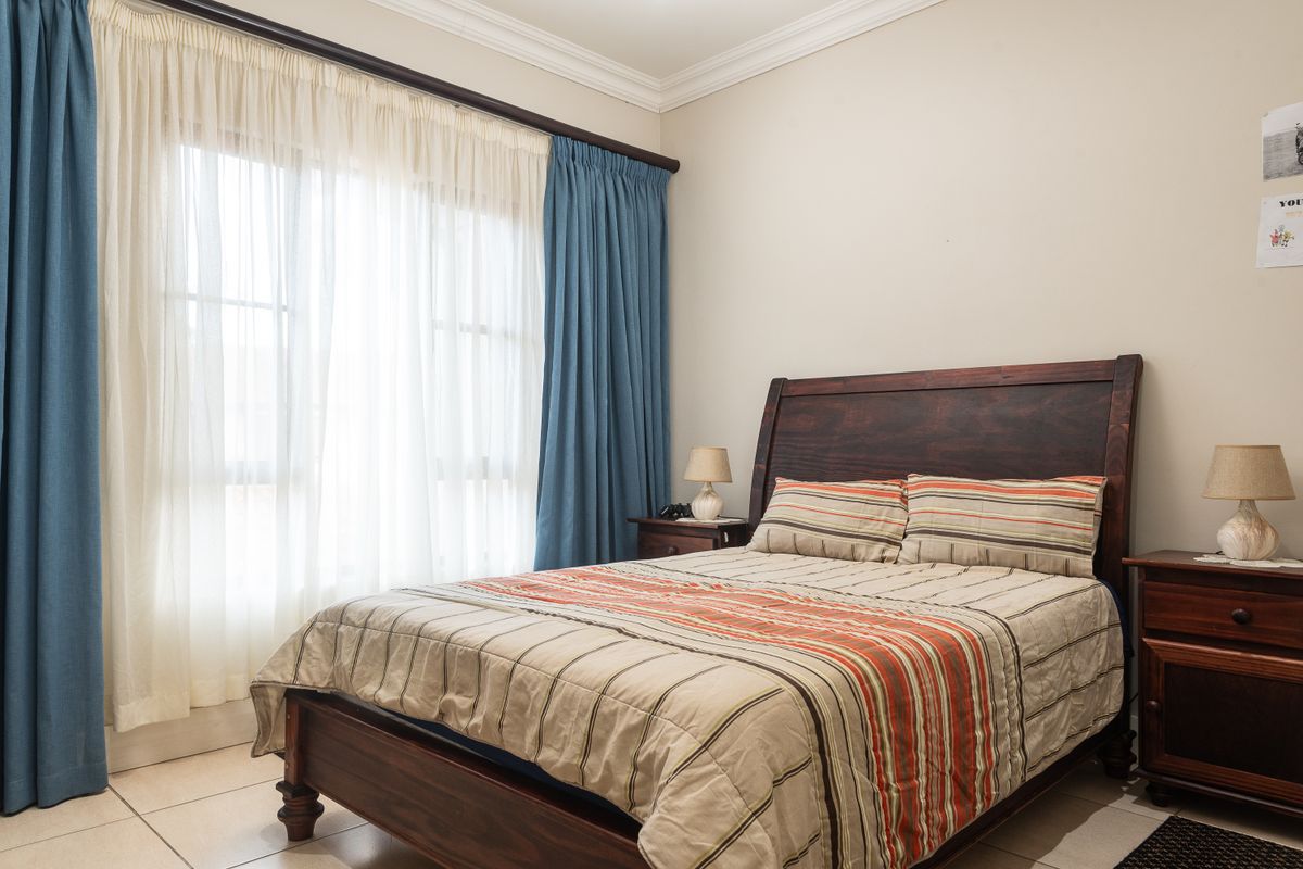 A well-lit bedroom featuring tiled flooring, crown molding, and a large window with curtain tracks.