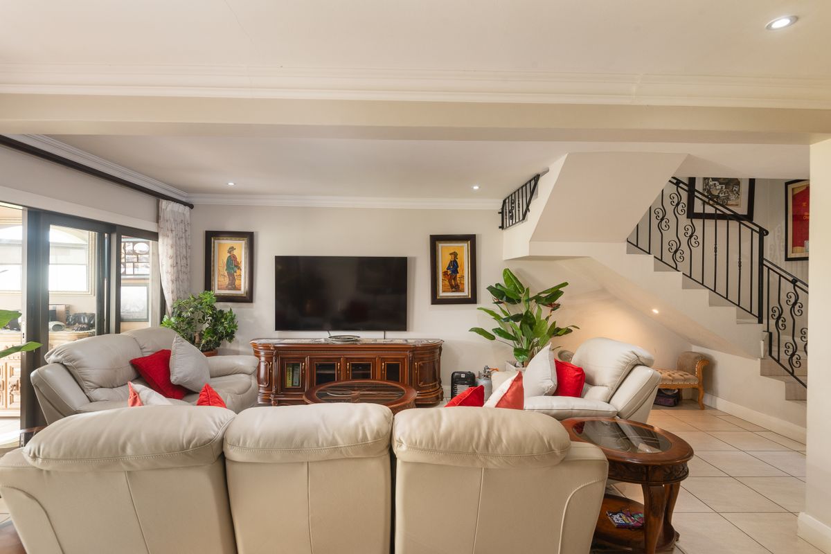A spacious living room featuring tiled flooring, recessed ceiling lighting, and a staircase with decorative wrought iron railings.
