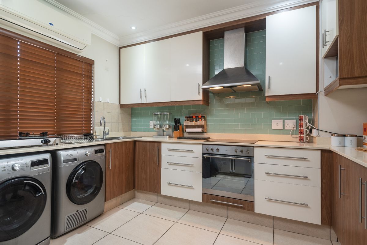 Modern kitchen featuring two-tone cabinetry, subway tile backsplash, built-in oven with extractor fan, and integrated laundry appliances.