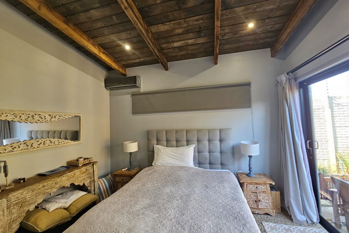 A well-maintained bedroom featuring a rustic exposed timber beam ceiling, integrated air conditioning unit, and direct access to an outdoor patio area.