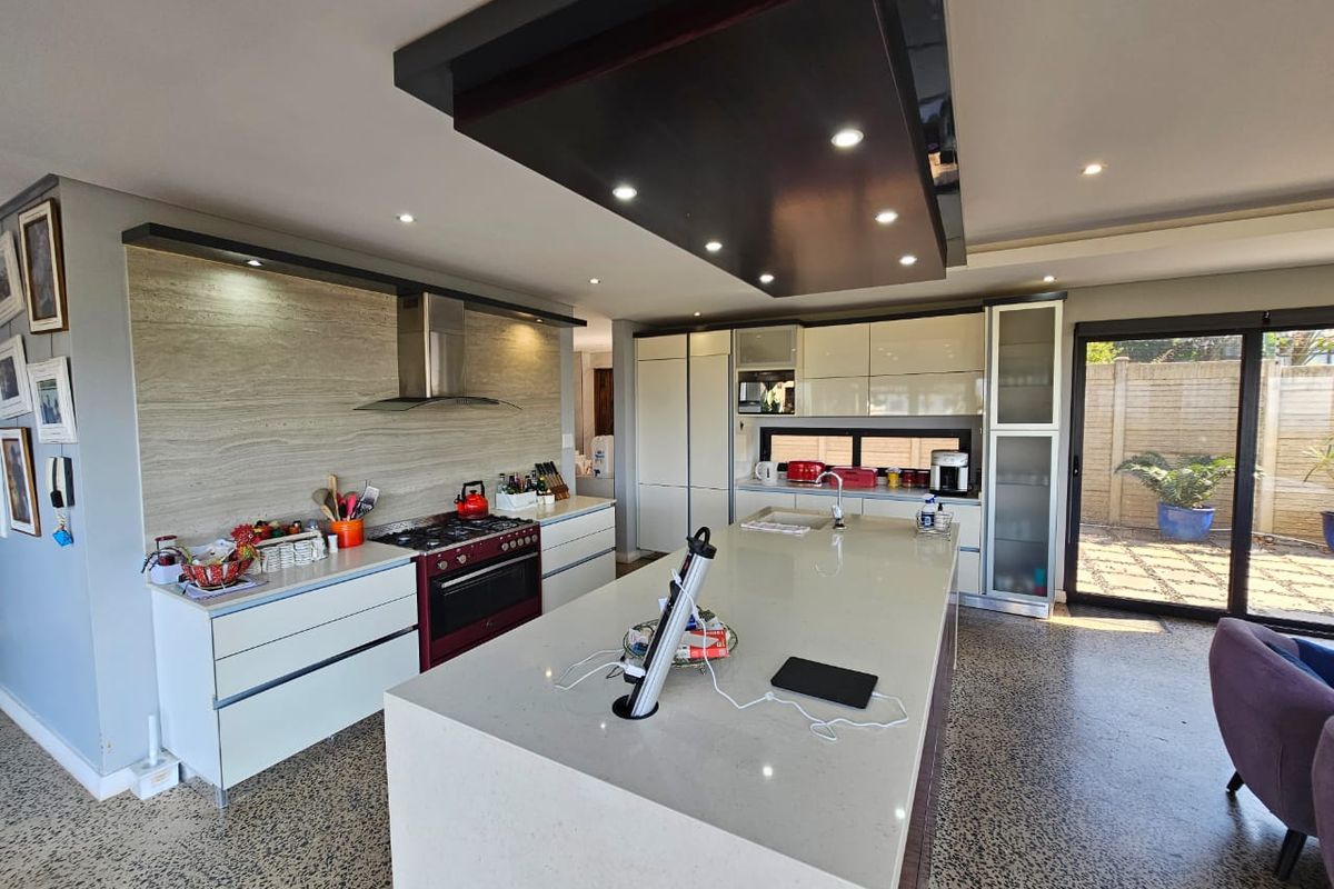 Modern kitchen featuring a large central island with stone countertops, integrated cabinetry, a built-in gas range, and a sleek overhead bulkhead with recessed lighting.
