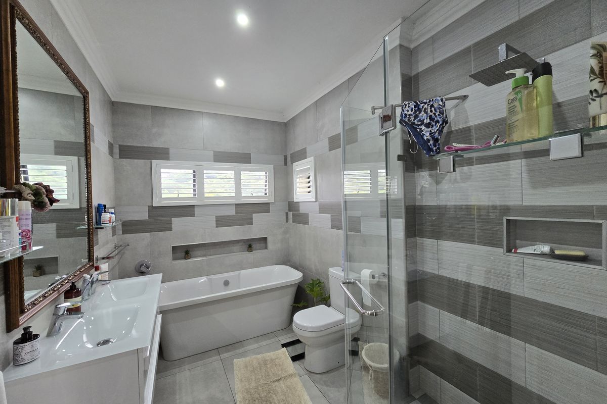 Modern bathroom featuring a freestanding bathtub, glass-enclosed walk-in shower, double vanity, and contemporary grey tiled walls with built-in recessed shelving.