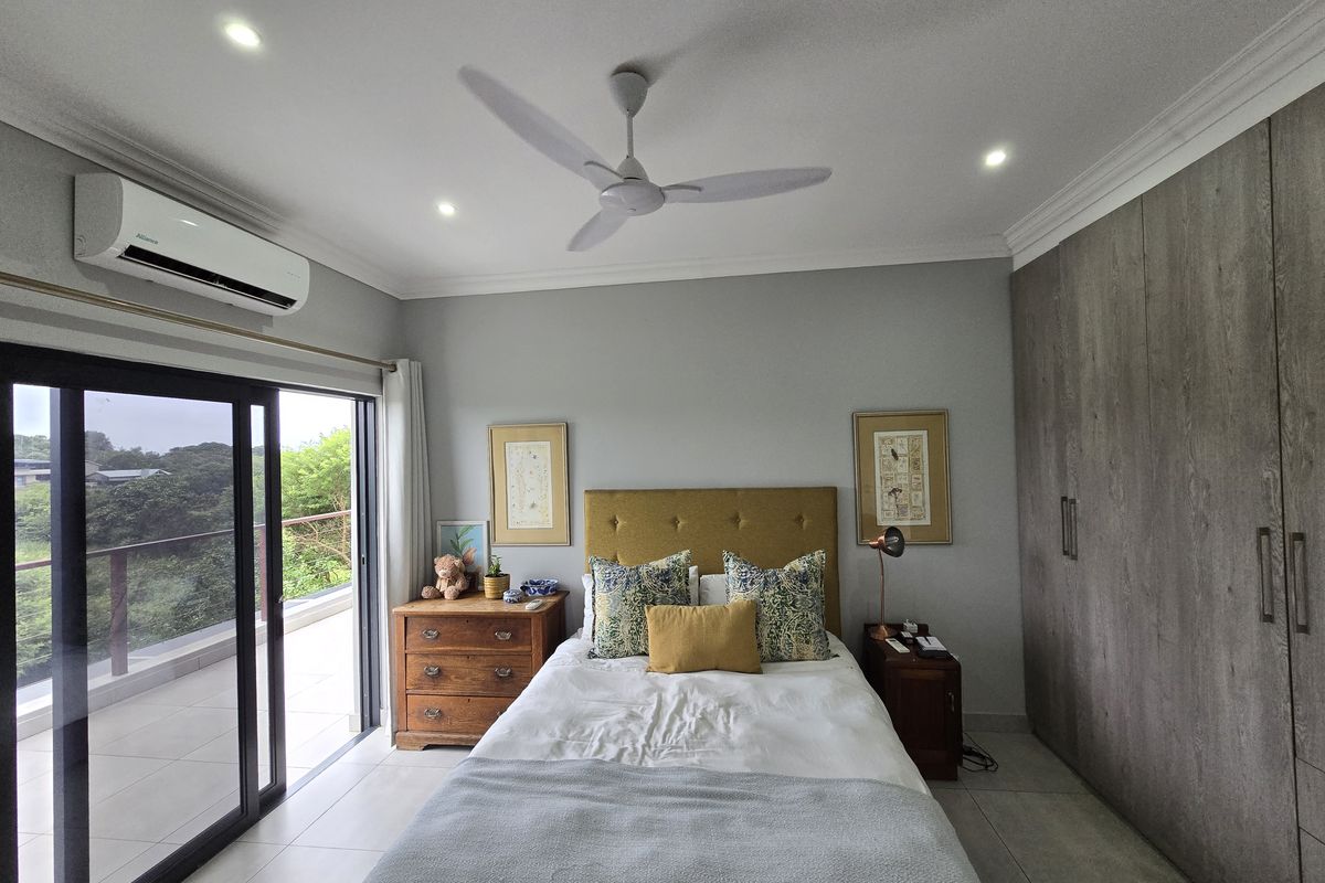 A well-maintained bedroom featuring built-in floor-to-ceiling wardrobes, a ceiling fan, recessed lighting, and sliding glass doors leading to a private balcony.