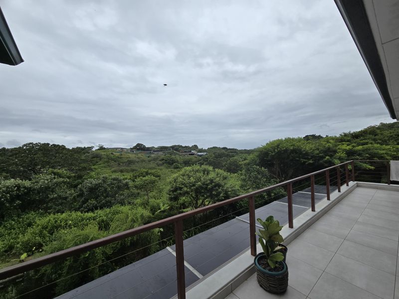 A spacious balcony featuring modern tiled flooring and a sleek timber and wire balustrade, offering expansive views over the surrounding natural landscape.