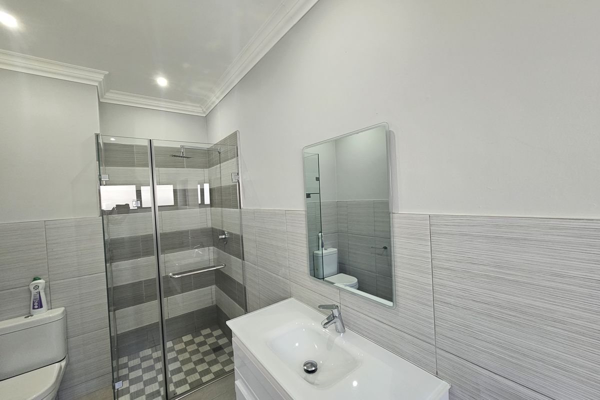 Modern bathroom featuring a glass-enclosed shower, contemporary vanity with basin, wall-mounted mirror, and neutral tiled finishes.