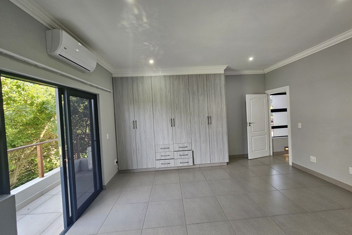 Spacious bedroom featuring built-in cupboards, tiled flooring, recessed lighting, and a wall-mounted air conditioning unit with direct access to a balcony.
