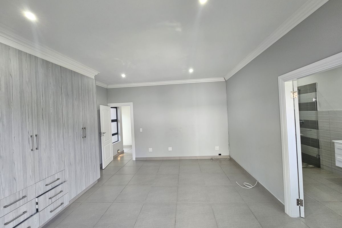 Spacious bedroom featuring built-in cupboards, tiled flooring, recessed ceiling lighting, and an en-suite bathroom entrance.