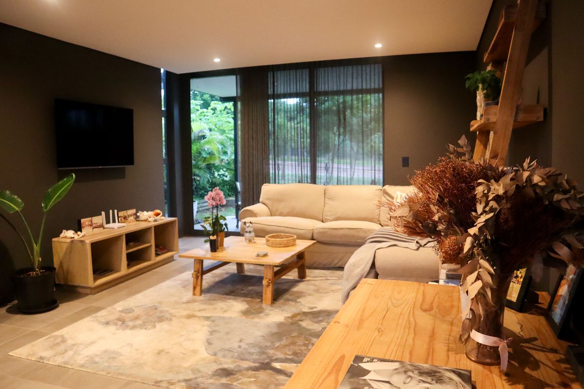 A modern, well-lit living room featuring dark accent walls, large floor-to-ceiling glass sliding doors, and tiled flooring, offering a seamless transition to the outdoor area.