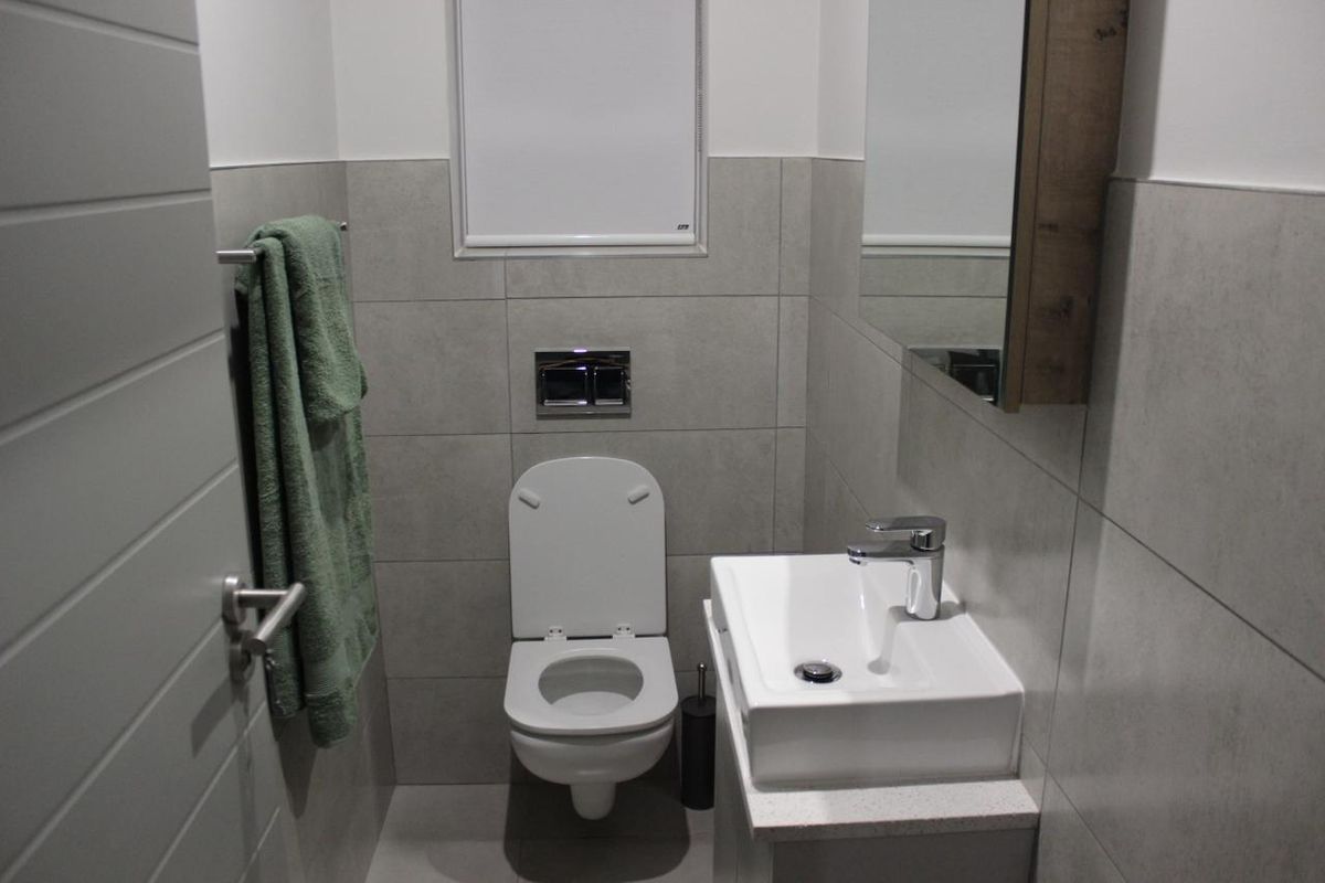 A modern, compact bathroom featuring a wall-mounted toilet, a sleek vanity basin with chrome tapware, and neutral grey wall tiling.