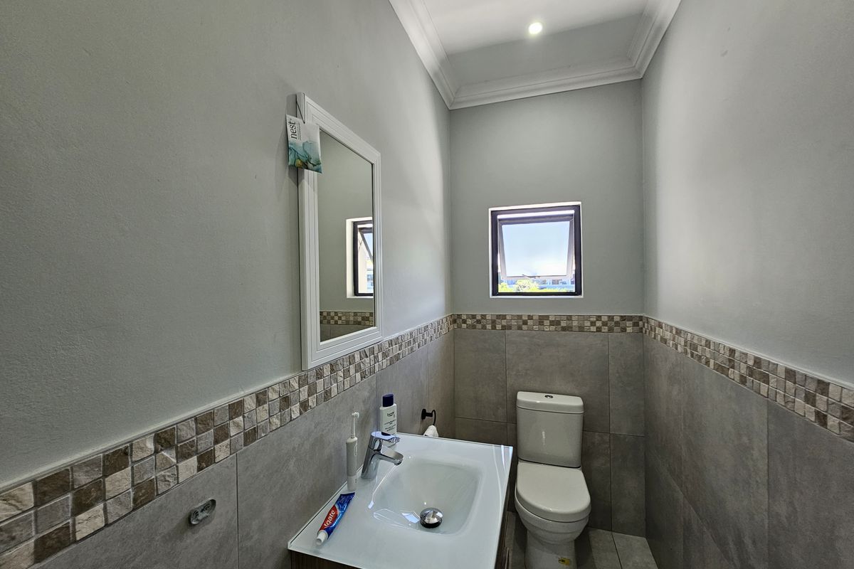 A compact bathroom featuring a modern vanity with a basin, a toilet, and neutral wall tiling with a decorative mosaic border.